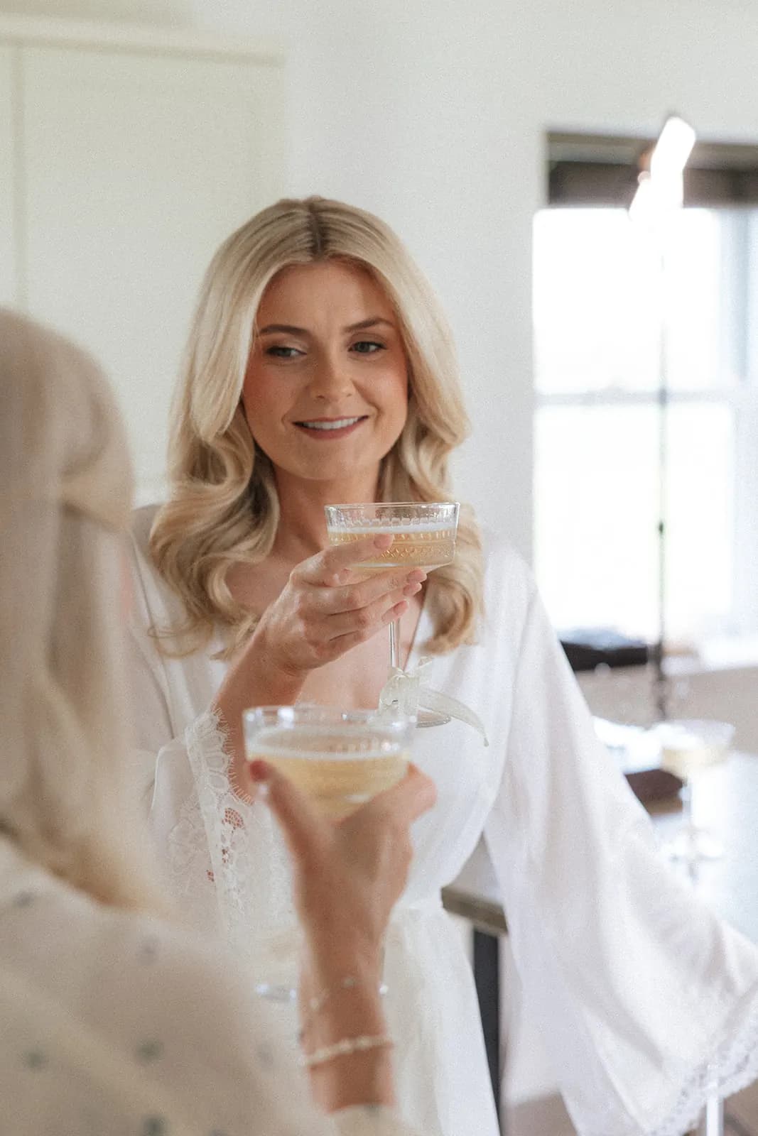 Smiling blonde bride with voluminous blow-dried waves and a coupe of champagne