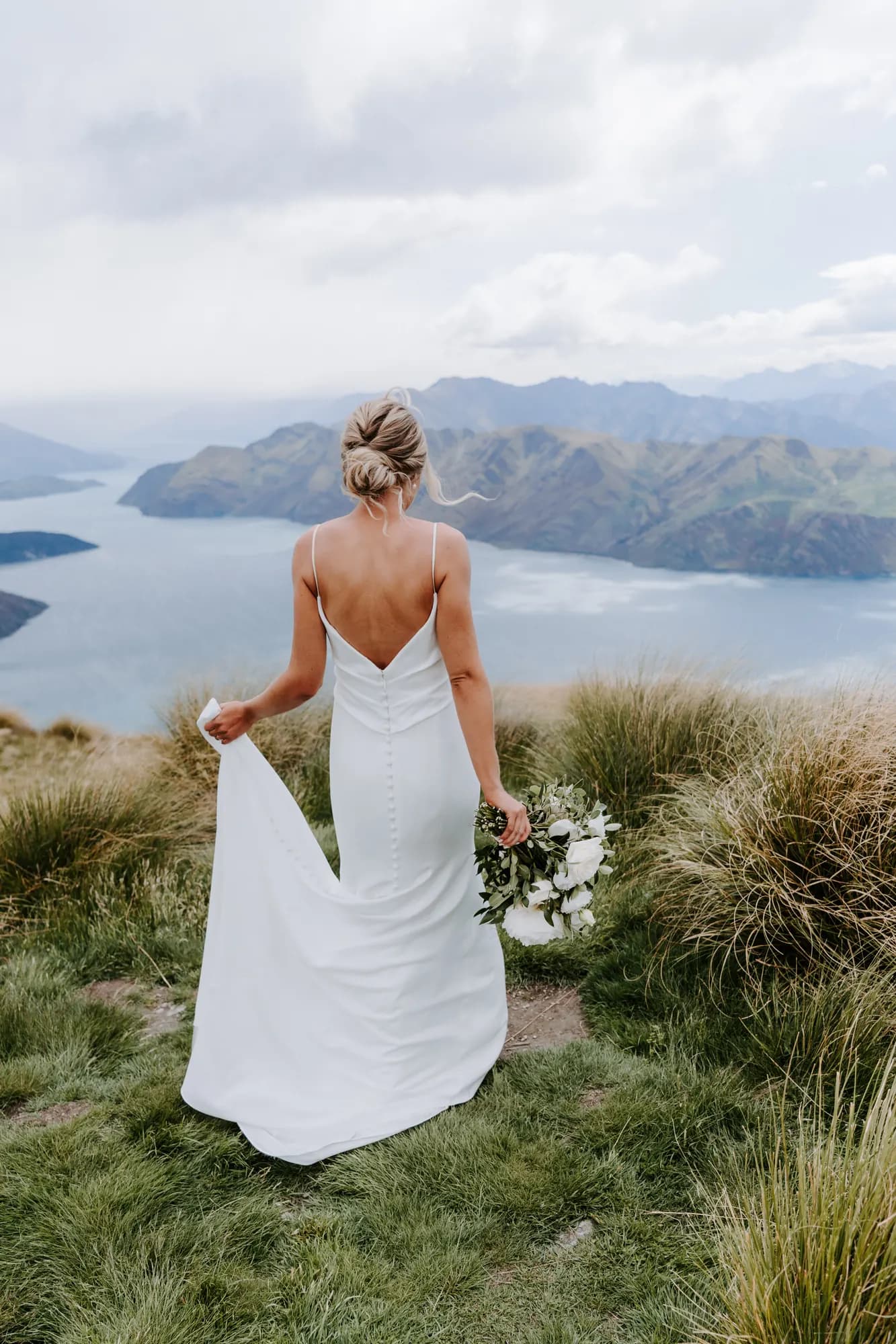 Bride from behind with a textured low chignon, looking out over a lake