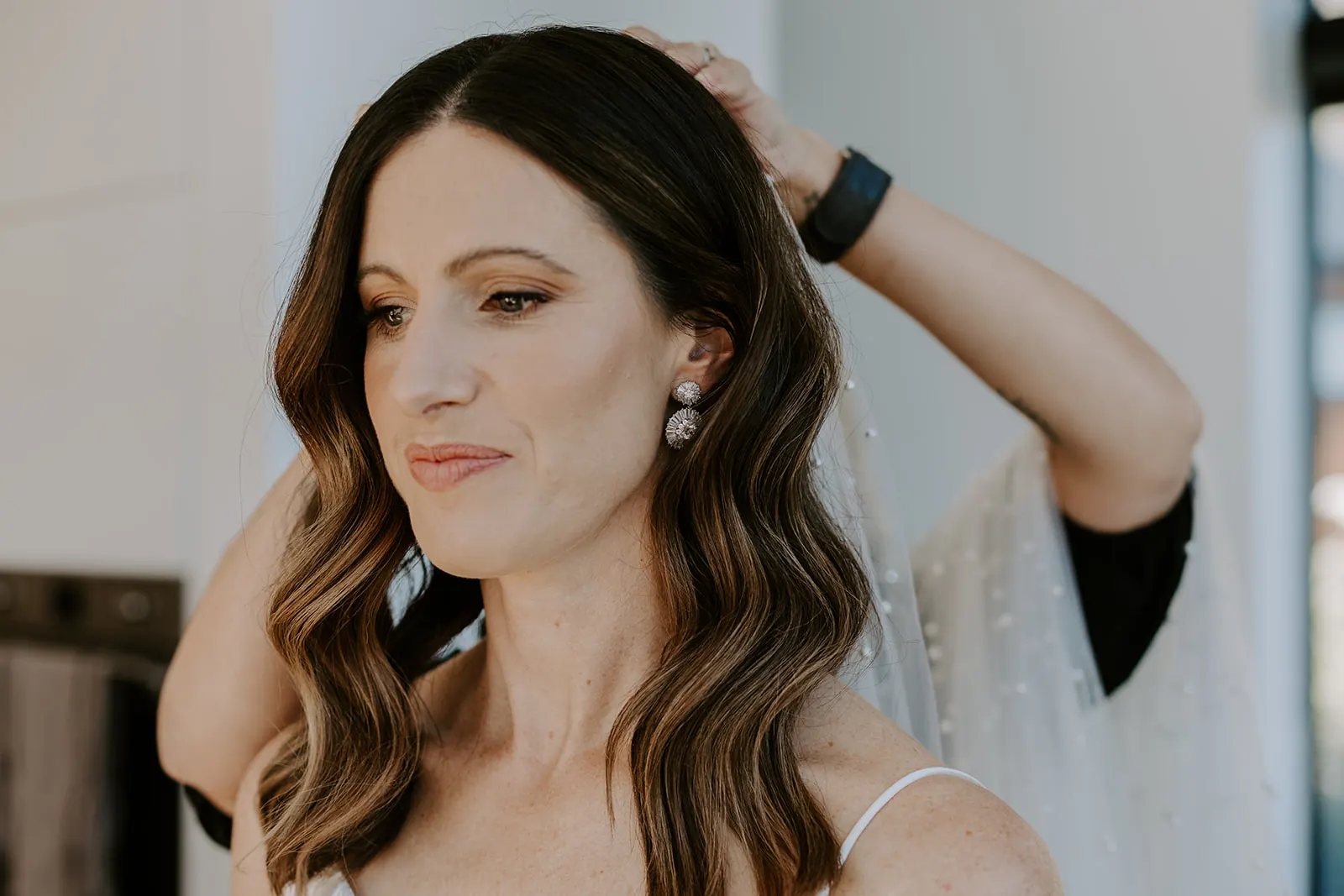 Bride with soft brunette waves fixing her veil